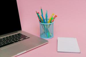 canetas para laptop e lápis de cor em suporte azul e adesivos brancos em rosa foto