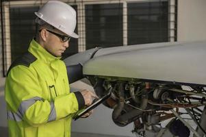 técnico consertando o motor do avião, engenharia aeroespacial masculina verificando motores de aeronaves, manutenção mecânica asiática inspeciona motor de avião foto