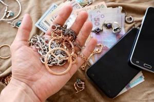 mão de saqueadores com monte de jóias roubadas, dinheiro e smartphones em tecido de pano de uniforme militar. saques por soldados russos nas cidades ucranianas durante a invasão russa na ucrânia foto