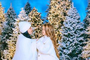 mãe asiática e sua filha caucasiana pela árvore de natal ao ar livre. amor, família, diversidade, conceito de férias foto