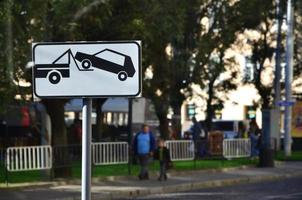 um sinal de estrada que mostra um caminhão de reboque de carro, que levanta um carro de passeio a bordo foto