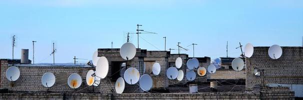 muitas antenas de televisão por satélite no telhado sob um céu azul foto