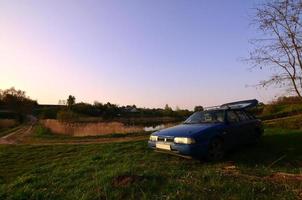 um carro azul sobre um fundo de uma paisagem rústica com um campo de cana selvagem e um pequeno lago. a família veio descansar na natureza perto do lago foto