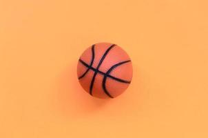 pequena bola laranja para jogo de esporte de basquete encontra-se no fundo de textura de papel de cor laranja pastel de moda em conceito mínimo foto