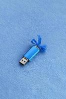 cartão de memória flash usb azul brilhante com um laço azul repousa sobre um cobertor de tecido de lã azul claro macio e peludo. design de presente feminino clássico para um cartão de memória foto