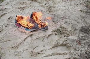 queima de tênis esportivos ou sapatos de ginástica em chamas na costa da praia. atleta queimado. esforço físico durante o conceito de treinamento foto