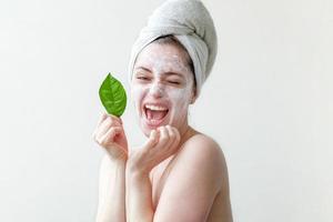 beleza mínima retrato mulher menina na toalha na cabeça aplicando máscara nutritiva branca ou creme no rosto, folha verde na mão isolado fundo branco. skincare limpeza conceito de spa cosmético orgânico eco. foto