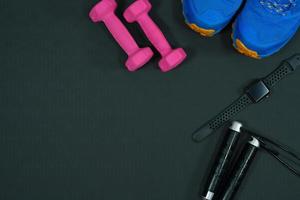 fundo rosa haltere e sapatos esportivos relógio inteligente pular corda no fundo de borracha preta conceito de fundo de equipamentos de fitness foto