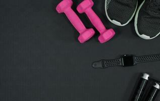 fundo rosa haltere e sapatos esportivos relógio inteligente pular corda no fundo de borracha preta conceito de fundo de equipamentos de fitness foto