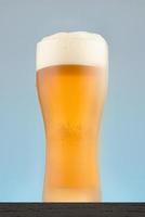 close-up de vidro de cerveja em um fundo azul. copo de cerveja enevoado com espuma. foto