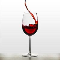 um pouco de vinho tinto em um copo de vinho. salpicos de vinho. água potável. álcool. isolado no fundo foto