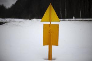 sinal amarelo na neve. poste de aço no chão. sinal de aviso. foto