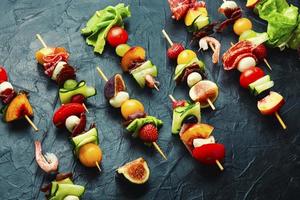 espetos de madeira com camarões, carne e frutas foto