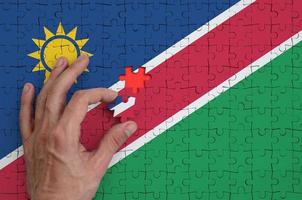 a bandeira da namíbia é retratada em um quebra-cabeça, que a mão do homem completa para dobrar foto