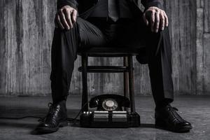 esperando por uma chamada importante. close-up de homem mandão em trajes formais, sentado na cadeira com telefone antiquado, perto de seus pés foto