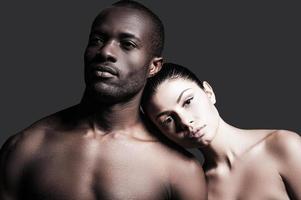 raças diferentes e um amor. retrato de homem africano sem camisa e mulher caucasiana, unindo-se um ao outro em pé contra um fundo cinza foto