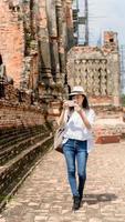 mulher hipster vestindo camisa branca e chapéu tirando foto pelo celular no templo ayutthaya tailândia, conceito de relaxamento de férias de viagem