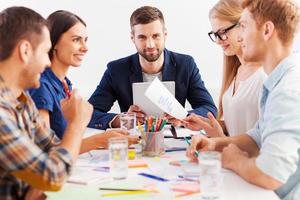 trabalhando em equipe. três empresários confiantes em roupas casuais inteligentes trabalhando juntos enquanto estão sentados à mesa foto