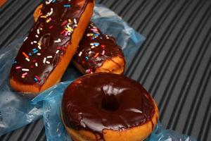 rosquinhas de chocolate e barras de donuts de chocolate cobertas com flocos de açúcar multicoloridos. colocado em um piso de alumínio cinza. foto