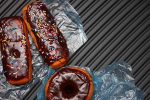 rosquinhas de chocolate e barras de donuts de chocolate cobertas com flocos de açúcar multicoloridos. colocado em um piso de alumínio cinza. foto