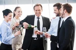 comemorando o sucesso. grupo de empresários segurando flautas com champanhe e sorrindo em pé perto um do outro dentro de casa foto