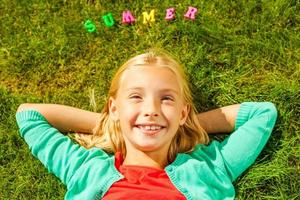 eu amo a vista superior de verão da menina bonitinha segurando as mãos atrás da cabeça e sorrindo enquanto estava deitado na grama verde com letras coloridas de plástico sobre a cabeça foto