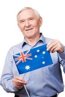 vovô da Austrália. alegre homem sênior segurando a bandeira da austrália e sorrindo para a câmera em pé contra um fundo branco foto