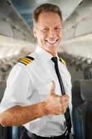 eu amo meu trabalho piloto masculino confiante de uniforme mostrando o polegar para cima e sorrindo enquanto está dentro do avião foto