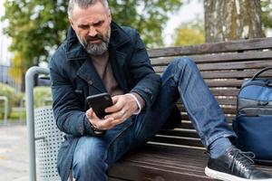 homem adulto sentado em um banco no parque olhando para um celular foto