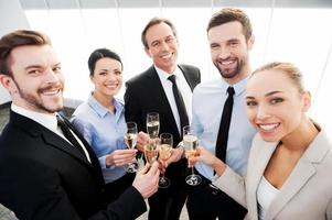 brinde ao sucesso. grupo de empresários brindando com champanhe e sorrindo em pé perto de cada um foto