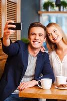 capturando os momentos brilhantes. lindo jovem casal amoroso se unindo no café enquanto homem fazendo selfie por telefone inteligente foto