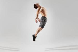 homem musculoso confiante com corpo perfeito pulando contra fundo branco foto