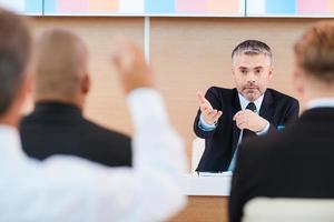 sim, você homem maduro confiante em trajes formais dando uma palavra a alguém da platéia enquanto está sentado na sala de conferências foto