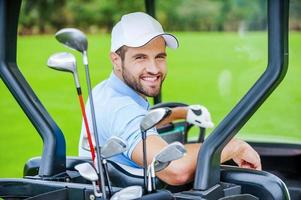 jogador de golfe no carrinho de golfe. vista traseira do jovem jogador de golfe masculino feliz dirigindo um carrinho de golfe e olhando por cima do ombro foto