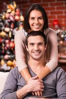 passar o natal juntos. lindo jovem casal apaixonado, unindo-se e sorrindo com a árvore de natal ao fundo foto