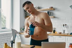 homem bonito apto preparando bebida de proteína em pé na cozinha foto