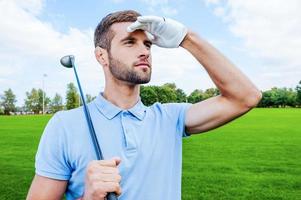 golfista confiante. confiante jovem golfista carregando motorista no ombro e desviar o olhar em pé no verde foto