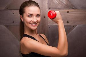 o esporte faz parte de sua vida. mulher musculosa segurando haltere e sorrindo em pé contra fundo de metal foto