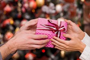 presente de Natal. close-up de casal segurando o presente de natal junto com a árvore de natal ao fundo foto