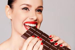 desejando que chocolate fosse uma fruta. close-up de uma linda mulher segurando o dedo em seus lábios vermelhos em pé contra um fundo cinza foto