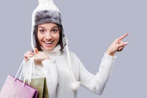tempo incrível para compras. mulheres jovens felizes em roupas quentes de inverno segurando pacotes com compras e apontando para fora em pé contra um fundo cinza