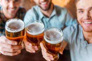 aplausos para o sucesso vista superior de três jovens felizes em roupas casuais brindando com cerveja enquanto estão sentados no bar juntos foto