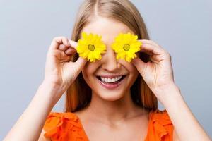 humor de verão. mulher jovem e bonita no vestido bonito segurando flores na frente de seus olhos em pé contra um fundo cinza foto