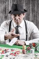 eu ganhei um homem sênior sério de camisa e suspensórios jogando suas cartas na mesa de pôquer e olhando para você foto