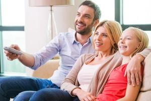 assistindo tv juntos. família feliz de três unindo-se e sorrindo enquanto está sentado no sofá e assistindo tv juntos