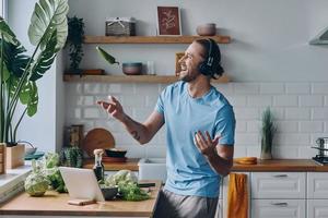 jovem feliz em fones de ouvido jogando um pimentão verde enquanto prepara comida na cozinha foto