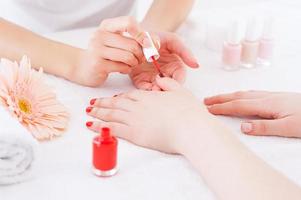 manicure em ação. close-up de manicure fazendo manicure vermelha para cliente do sexo feminino foto