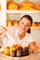 biscoitos artesanais para venda. mulher jovem e bonita no avental carregando prato com biscoitos frescos e sorrindo em pé na padaria foto