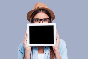 jovem com seu tablet digital. mulheres jovens segurando seu tablet digital na frente de seu rosto em pé contra um fundo cinza foto