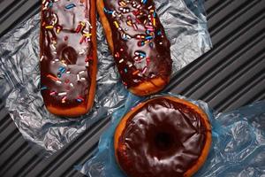 rosquinhas de chocolate e barras de donuts de chocolate cobertas com flocos de açúcar multicoloridos. colocado em um piso de alumínio cinza. foto